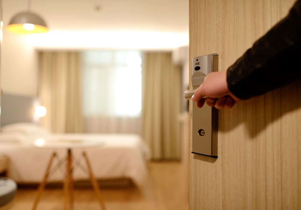 A hand opens the door to an empty hotel room