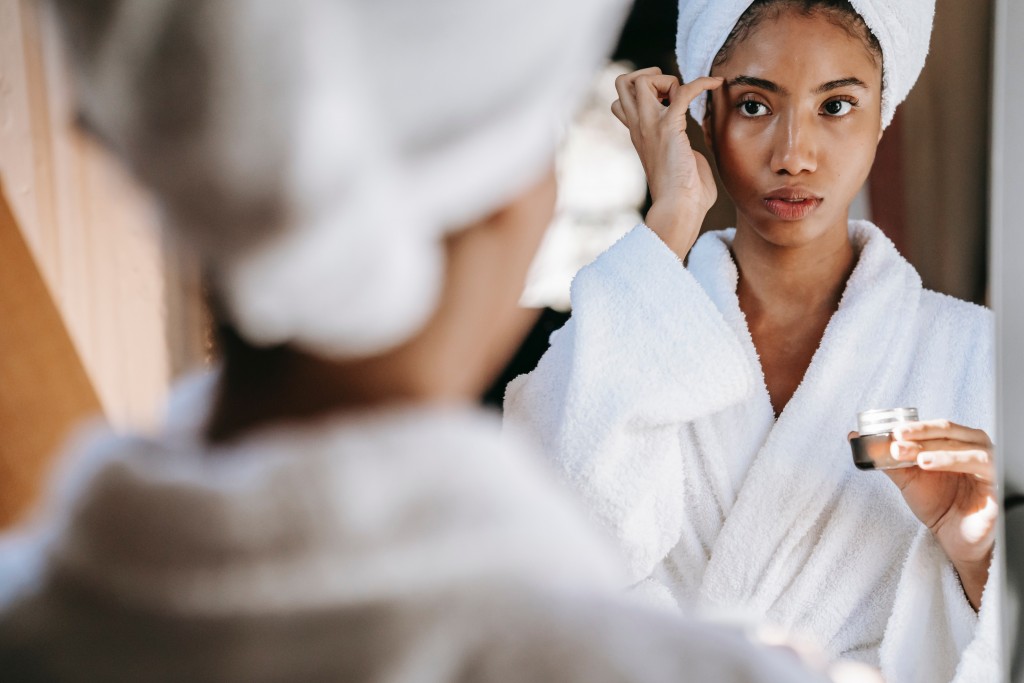 A woman applies a skincare product to her face while looking at the mirror
